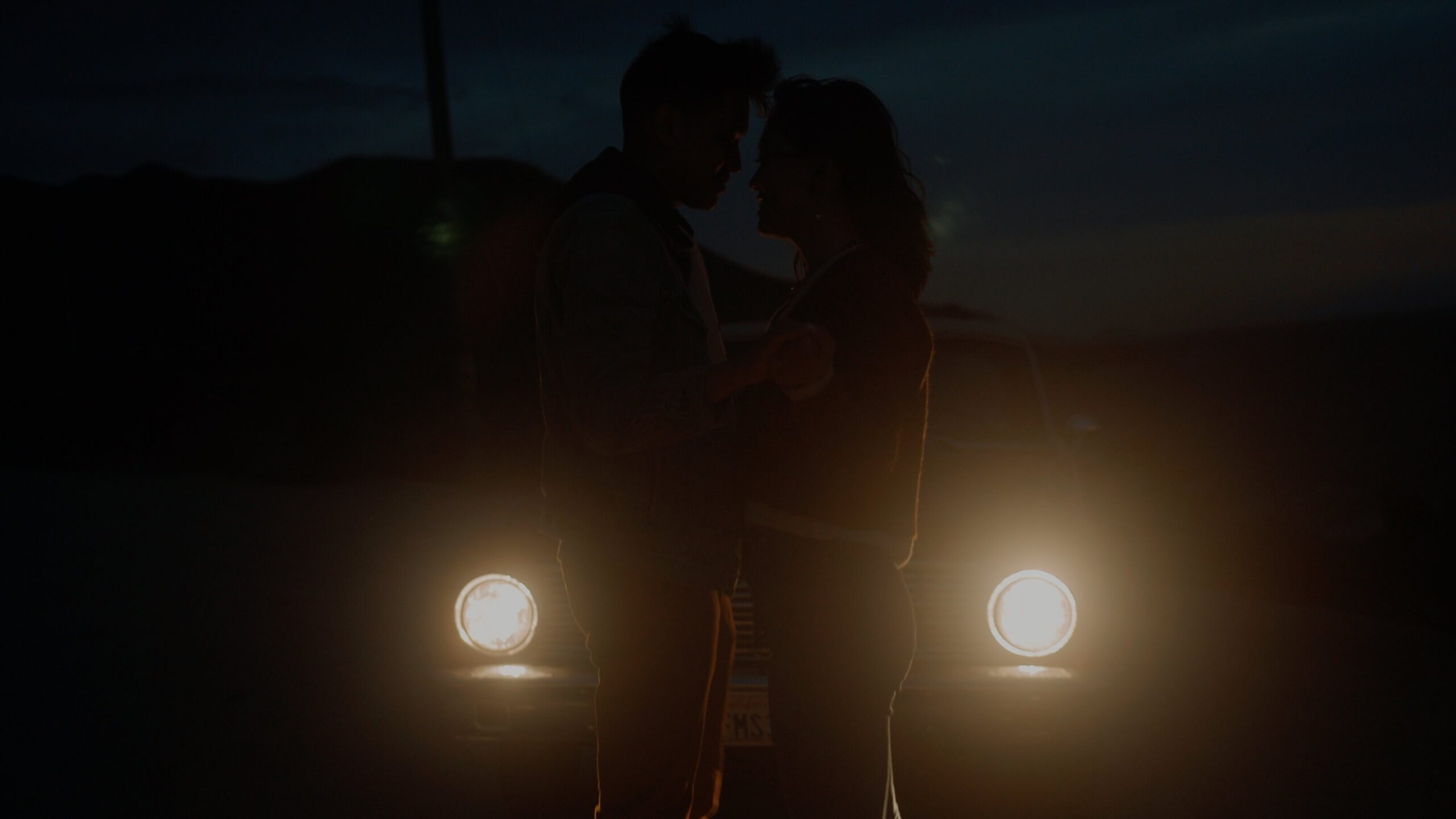 a couple holding hands in front of a car at night
