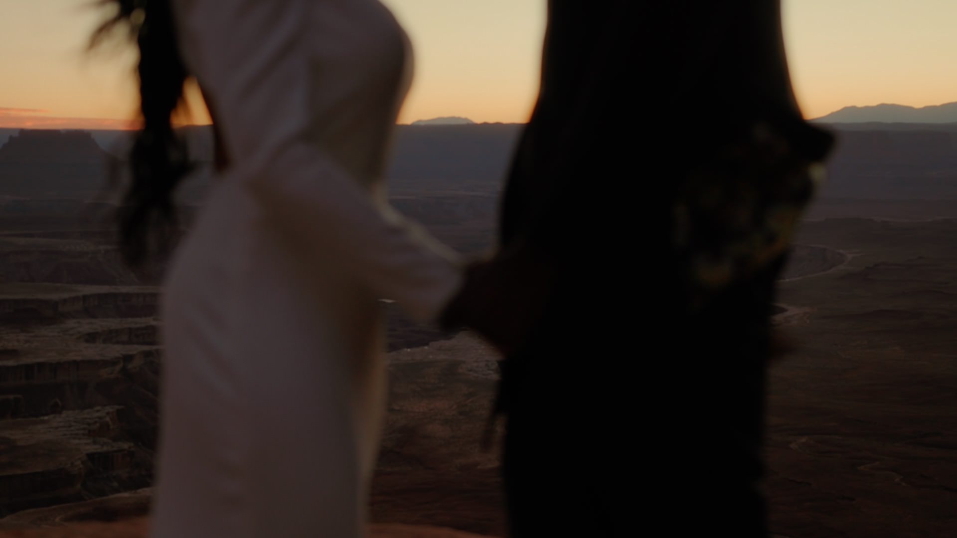 a man and woman holding hands standing over a cliff at canyonlands national park